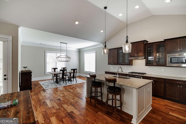 kitchen with sink, a kitchen breakfast bar, an island with sink, stainless steel appliances, and light stone countertops