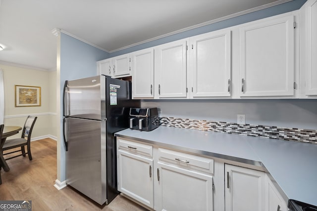 kitchen with stainless steel refrigerator, white cabinets, decorative backsplash, ornamental molding, and light wood-type flooring