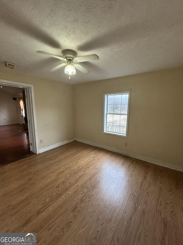 spare room featuring a textured ceiling, wood finished floors, a ceiling fan, and baseboards