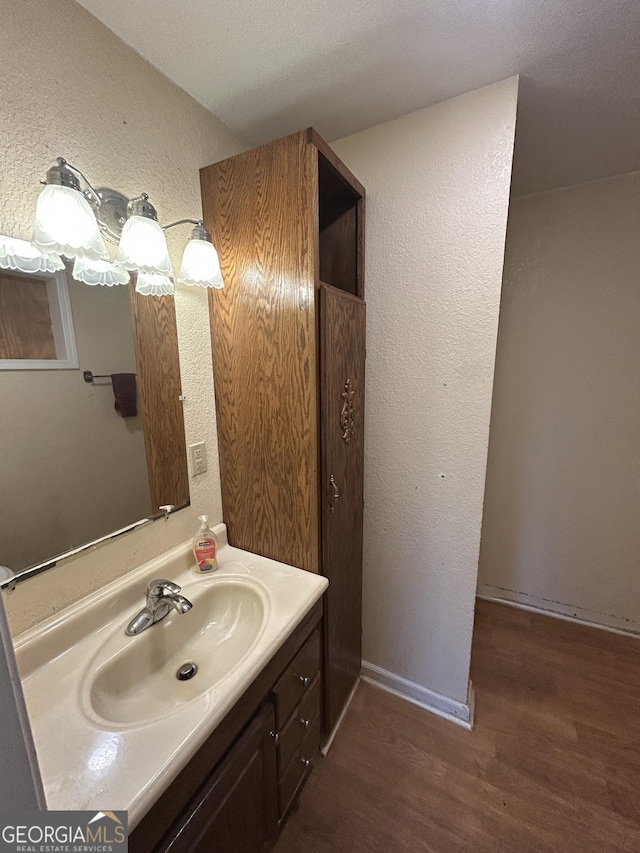 bathroom with a textured wall, baseboards, wood finished floors, and vanity