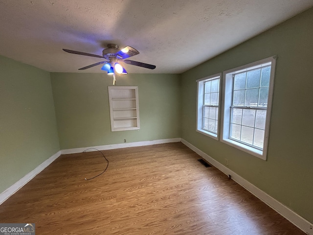 empty room with a textured ceiling, ceiling fan, visible vents, baseboards, and light wood finished floors