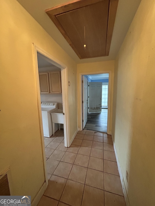 hall with washer / clothes dryer, a raised ceiling, attic access, light tile patterned flooring, and baseboards