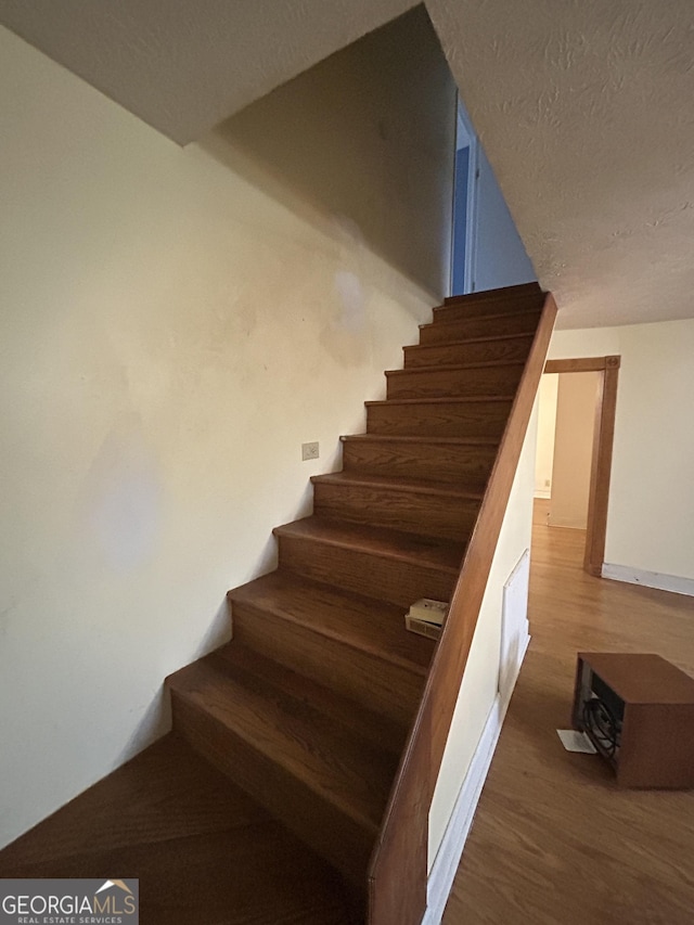 stairs with a textured ceiling and wood finished floors