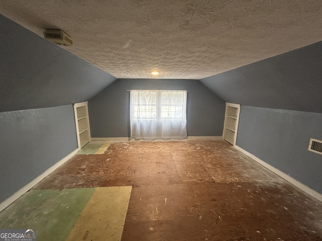 additional living space with a textured ceiling, visible vents, baseboards, vaulted ceiling, and built in features