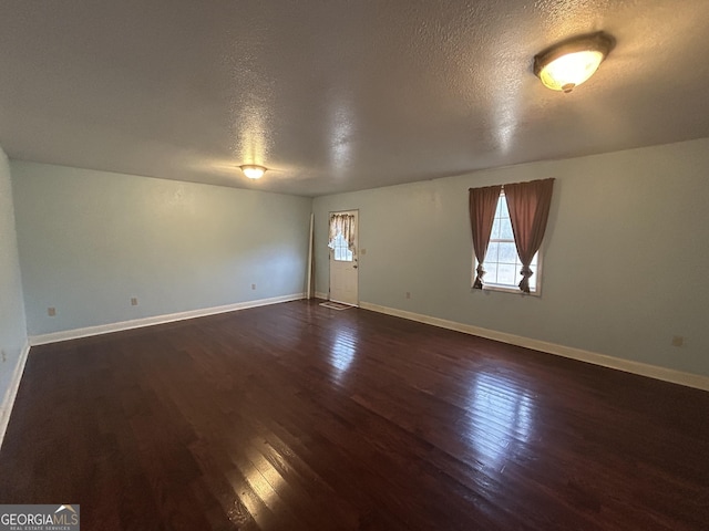 unfurnished room featuring baseboards, dark wood finished floors, and a textured ceiling