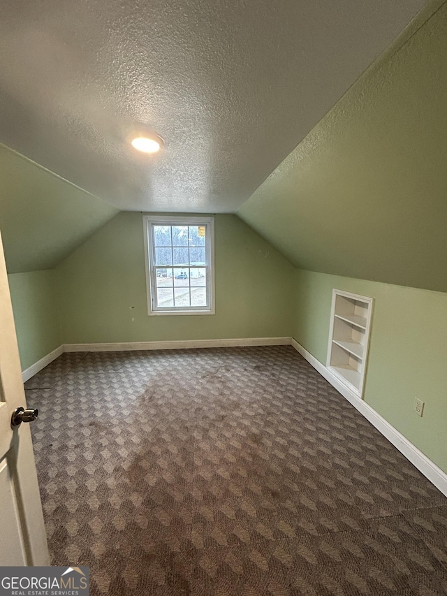 bonus room with a textured ceiling, dark colored carpet, baseboards, and built in features