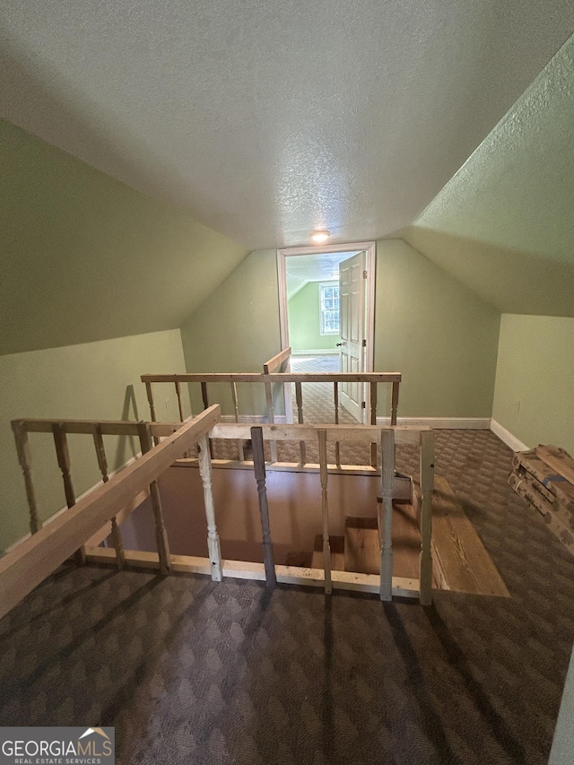 bonus room featuring lofted ceiling, dark carpet, a textured ceiling, and baseboards