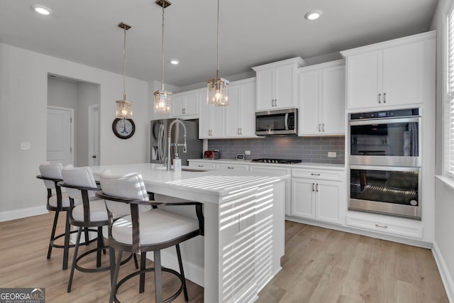 kitchen featuring hanging light fixtures, stainless steel appliances, tasteful backsplash, an island with sink, and white cabinets