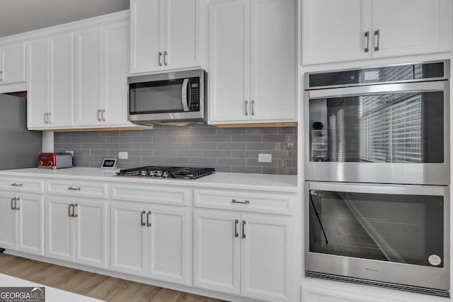 kitchen featuring white cabinetry, appliances with stainless steel finishes, light wood-type flooring, and backsplash