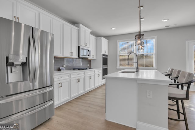 kitchen with sink, decorative light fixtures, a center island with sink, stainless steel appliances, and white cabinets