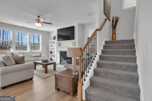 720 Lanarck Way, Peachtree City, GA 30269 - living room featuring stairs, ceiling fan, light wood finished floors, and a glass covered fireplace