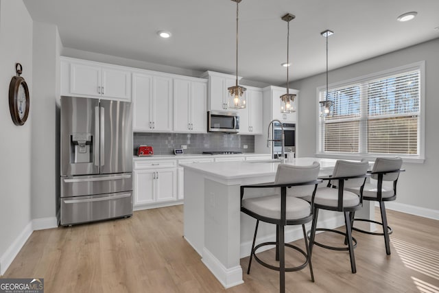 kitchen with sink, an island with sink, pendant lighting, stainless steel appliances, and white cabinets