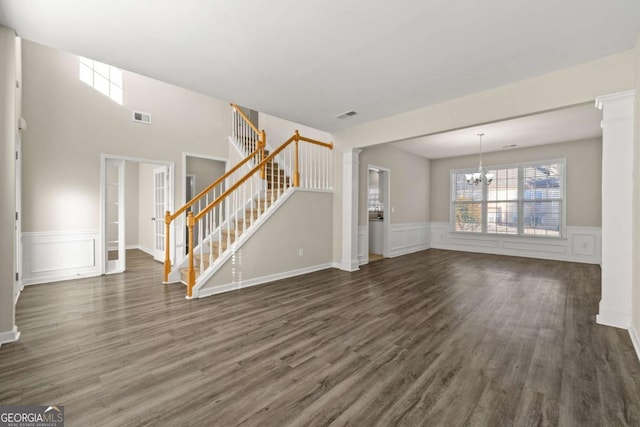 unfurnished living room with dark hardwood / wood-style floors, a chandelier, and decorative columns