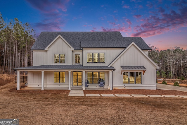 back of house at dusk with a yard, a shingled roof, and board and batten siding