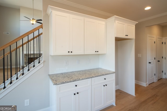 kitchen featuring light hardwood / wood-style flooring, ceiling fan, light stone counters, white cabinets, and decorative backsplash