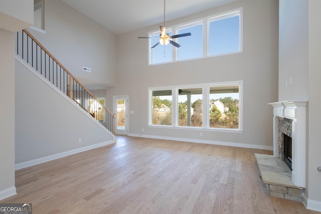 unfurnished living room featuring a high ceiling, ceiling fan, light wood-type flooring, and a fireplace