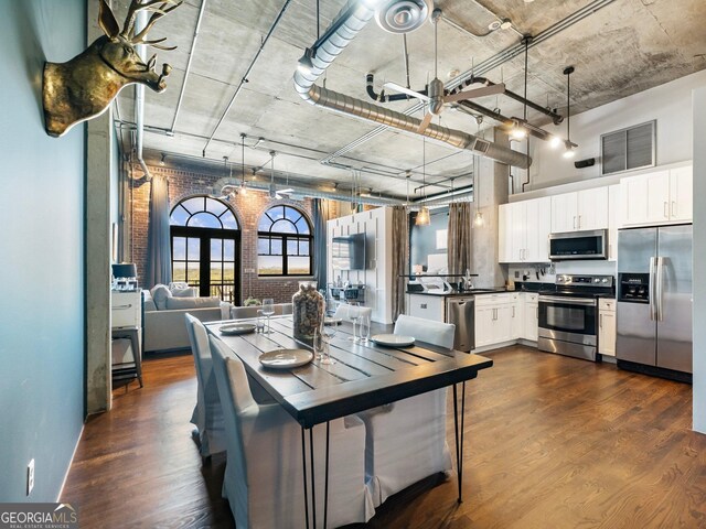 kitchen with brick wall, decorative light fixtures, white cabinetry, stainless steel appliances, and dark wood-type flooring