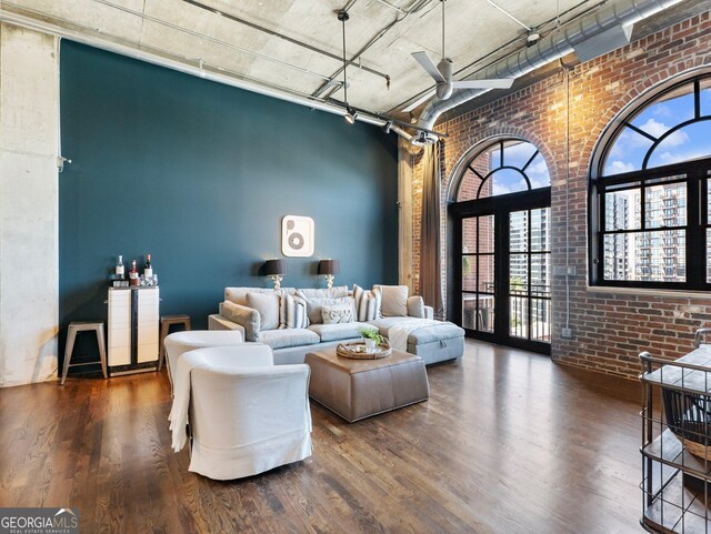 living room featuring dark wood-type flooring, a towering ceiling, and brick wall