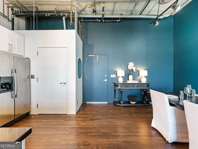 interior space with a towering ceiling, stainless steel fridge, dark hardwood / wood-style flooring, and white cabinets