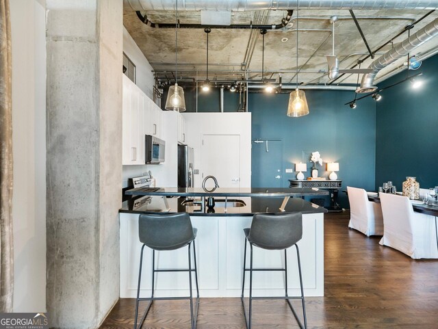 kitchen featuring dark wood-type flooring, white cabinetry, stainless steel appliances, and a breakfast bar area