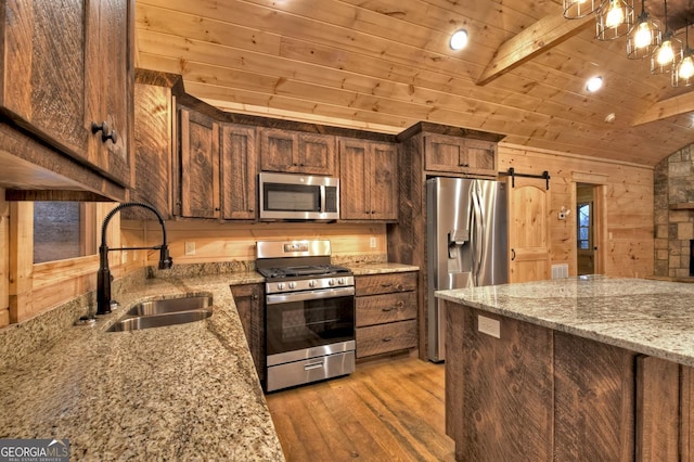 kitchen with sink, light stone counters, wooden ceiling, appliances with stainless steel finishes, and a barn door