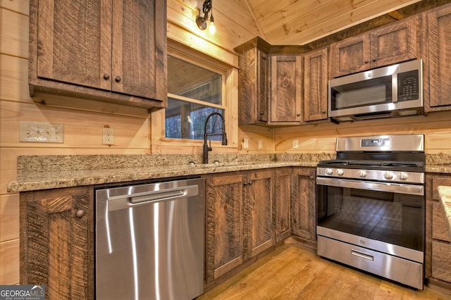 kitchen featuring sink, light hardwood / wood-style flooring, appliances with stainless steel finishes, wooden walls, and light stone countertops