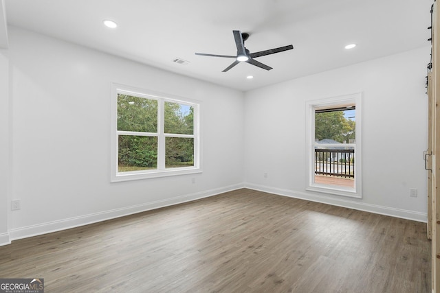 empty room featuring hardwood / wood-style flooring, a barn door, and ceiling fan