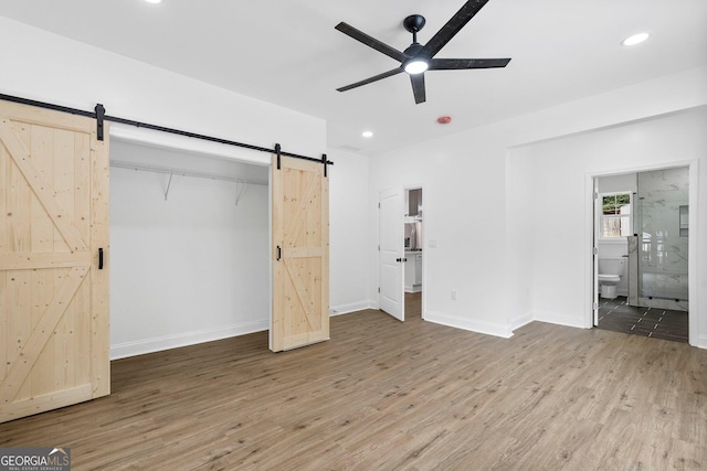 unfurnished bedroom with hardwood / wood-style flooring, ceiling fan, connected bathroom, a barn door, and a closet