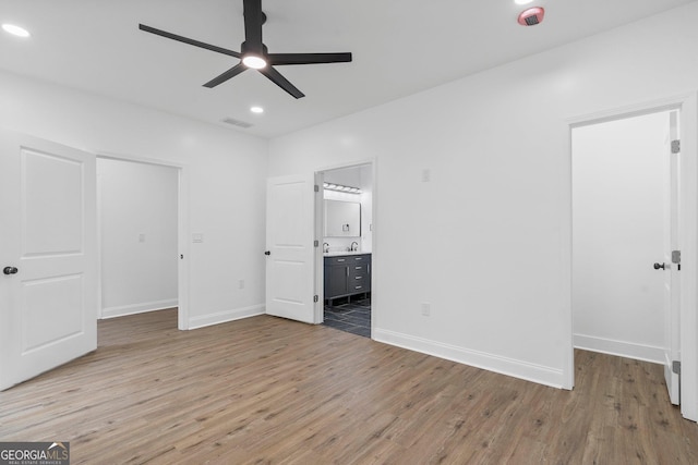 unfurnished bedroom featuring ensuite bathroom, a walk in closet, hardwood / wood-style floors, and ceiling fan