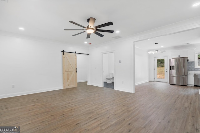 unfurnished living room featuring crown molding, wood-type flooring, a barn door, and ceiling fan