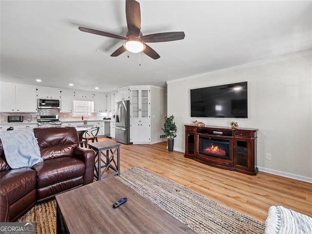 living room with ornamental molding, ceiling fan, and light wood-type flooring