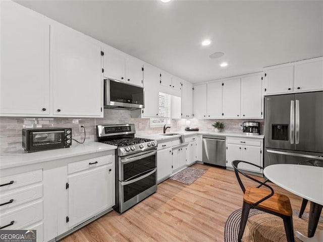 kitchen with white cabinetry, stainless steel appliances, light hardwood / wood-style flooring, and backsplash