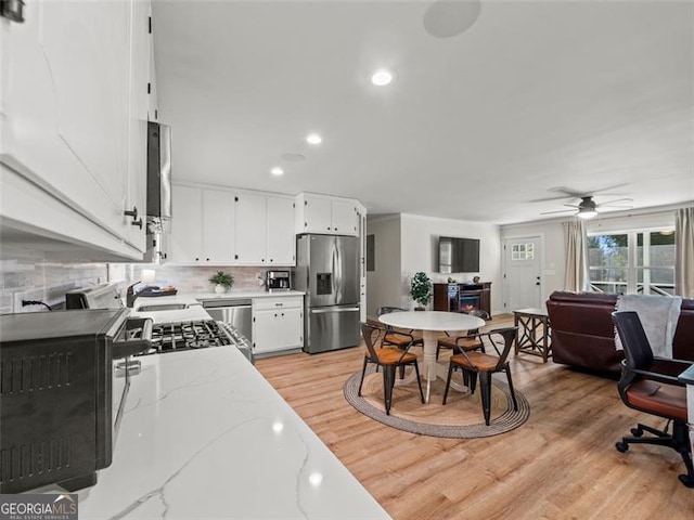 kitchen featuring light stone counters, light wood-type flooring, appliances with stainless steel finishes, white cabinets, and backsplash