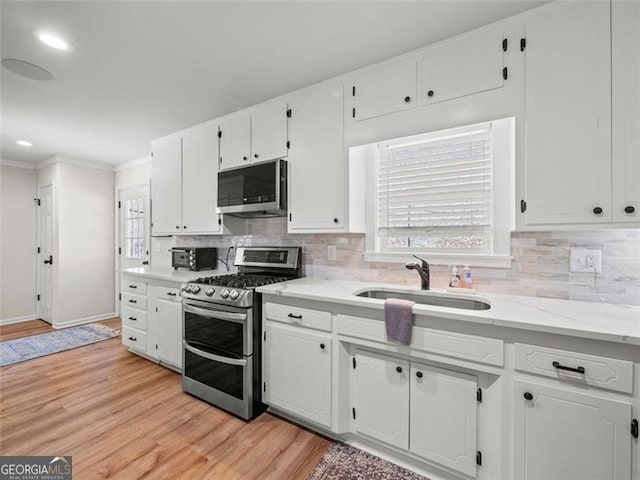 kitchen featuring sink, white cabinetry, light hardwood / wood-style flooring, stainless steel appliances, and backsplash