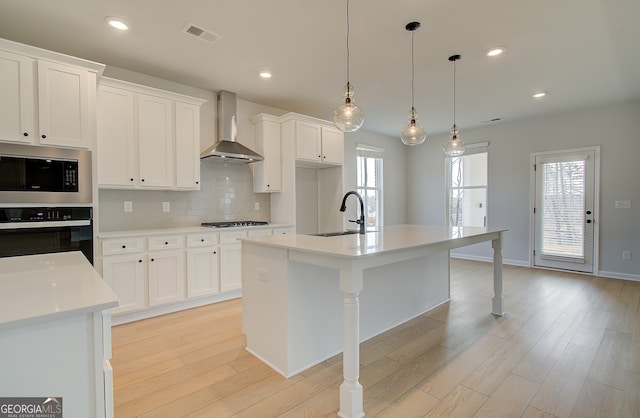 kitchen featuring stainless steel microwave, backsplash, wall oven, wall chimney range hood, and a sink