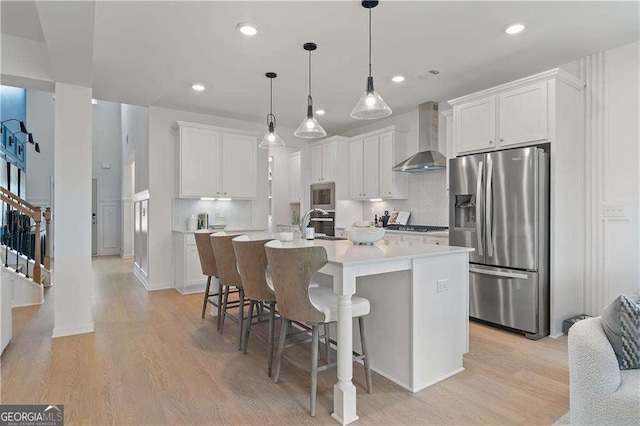 kitchen featuring white cabinetry, wall chimney range hood, a kitchen island with sink, and stainless steel appliances