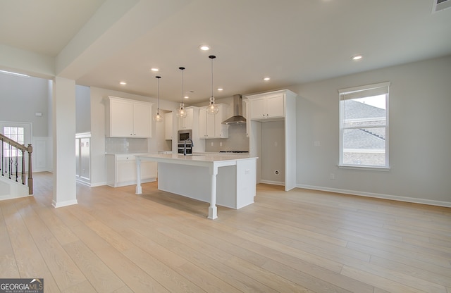 kitchen featuring a center island with sink, light wood-style flooring, recessed lighting, light countertops, and wall chimney exhaust hood