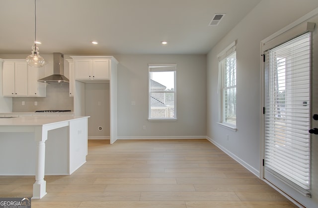 kitchen featuring visible vents, light countertops, light wood-style floors, wall chimney range hood, and backsplash