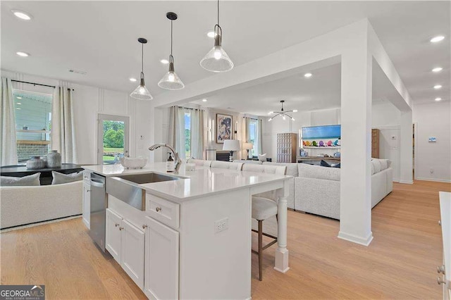 kitchen with sink, decorative light fixtures, a center island with sink, light hardwood / wood-style floors, and white cabinets