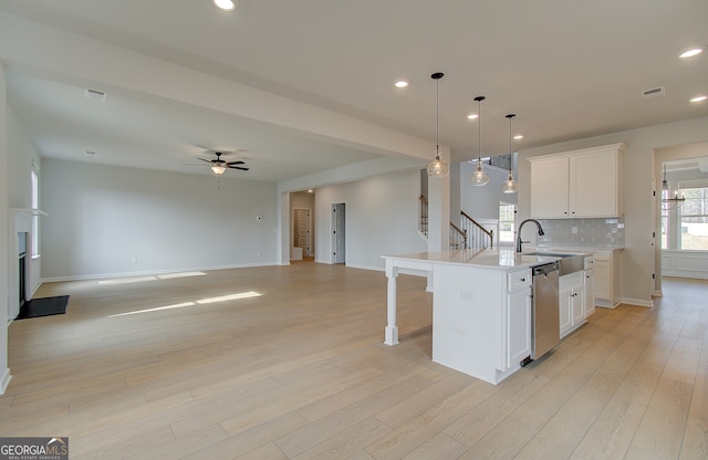 kitchen with tasteful backsplash, light countertops, light wood-style flooring, white cabinets, and stainless steel dishwasher