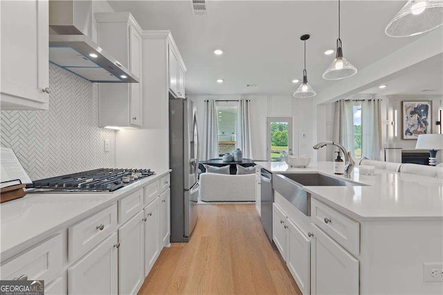 kitchen featuring sink, wall chimney range hood, pendant lighting, stainless steel appliances, and white cabinets