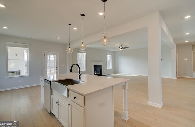 kitchen with light wood-type flooring, a sink, open floor plan, a glass covered fireplace, and dishwasher