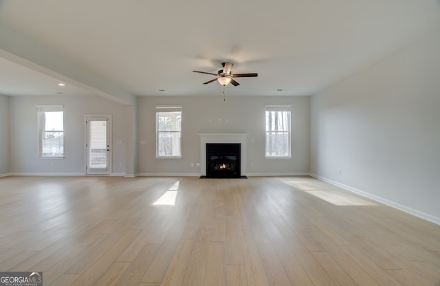 unfurnished living room with light wood finished floors, a warm lit fireplace, baseboards, and a wealth of natural light