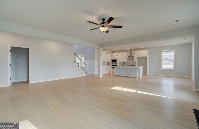 unfurnished living room with stairway, visible vents, a ceiling fan, and light wood finished floors