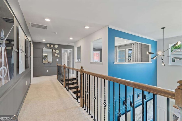 hall featuring crown molding, light carpet, and a notable chandelier