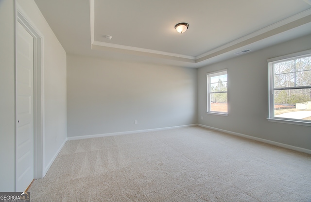 empty room with baseboards, visible vents, carpet floors, a tray ceiling, and crown molding