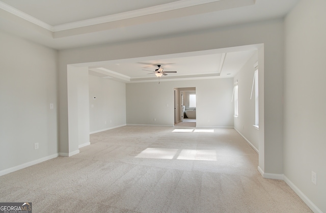 spare room with ornamental molding, a ceiling fan, a tray ceiling, baseboards, and light colored carpet