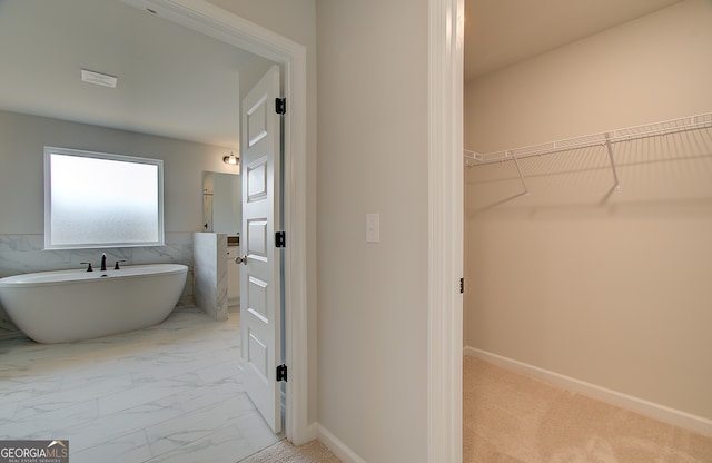 bathroom featuring a walk in closet, marble finish floor, tile walls, baseboards, and a soaking tub