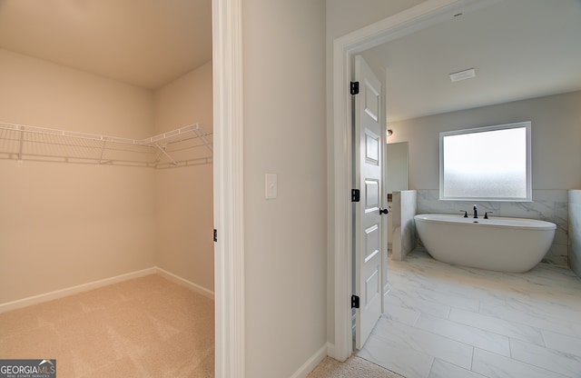 bathroom with baseboards, a freestanding bath, marble finish floor, and a spacious closet