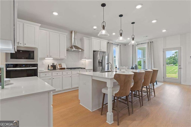 kitchen featuring white cabinets, black appliances, wall chimney exhaust hood, and a center island with sink